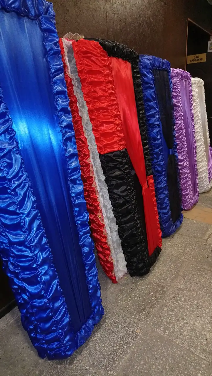 Обитые тканью гробы разных цветов в выставочном помещении