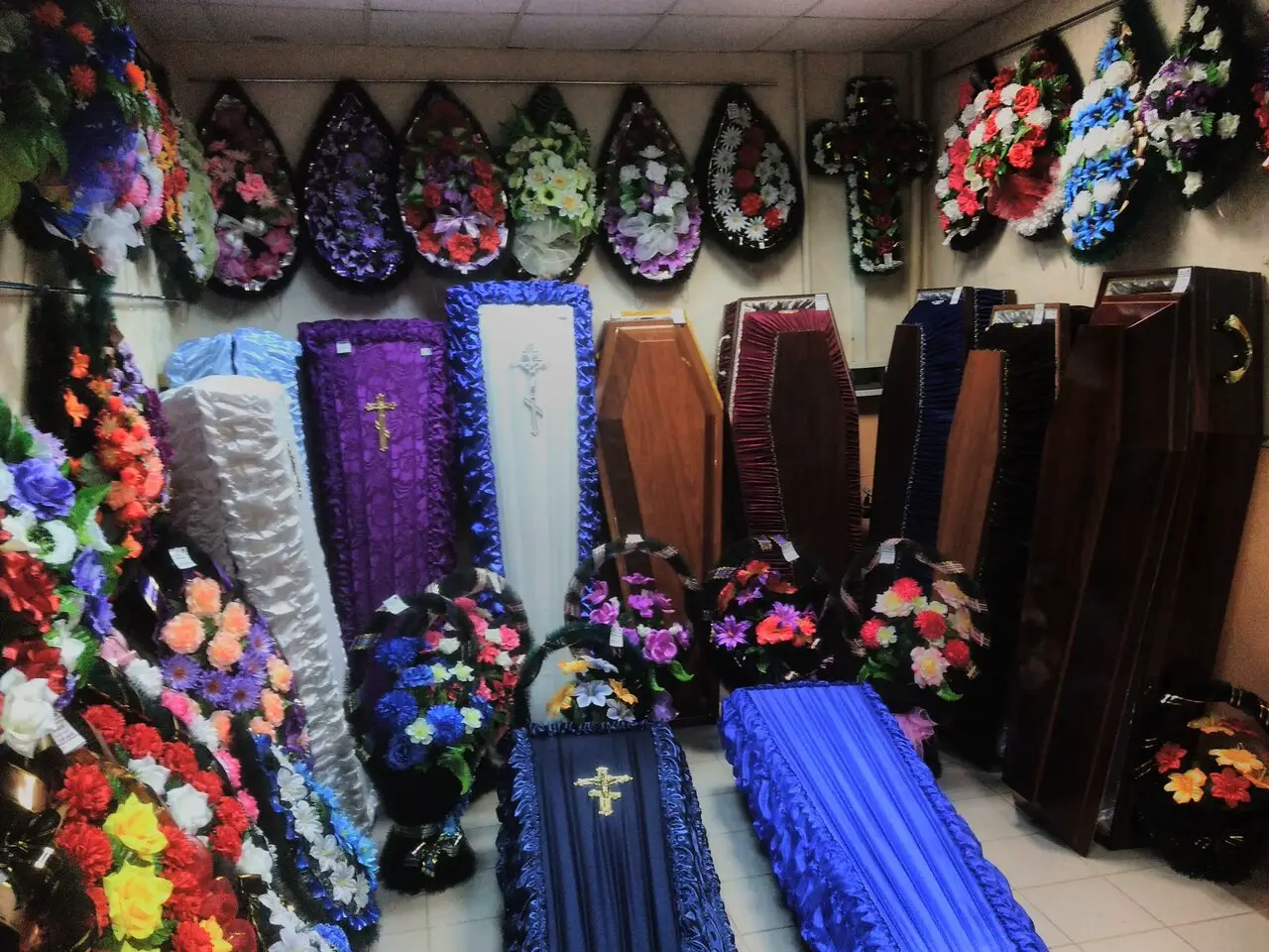 Помещение с гробами и траурными венками разных форм и цветов